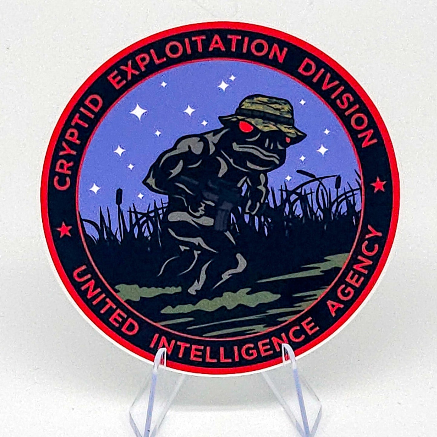 Circular sticker with a frog in a hat and carrying a rifle, surrounded by text on a white background