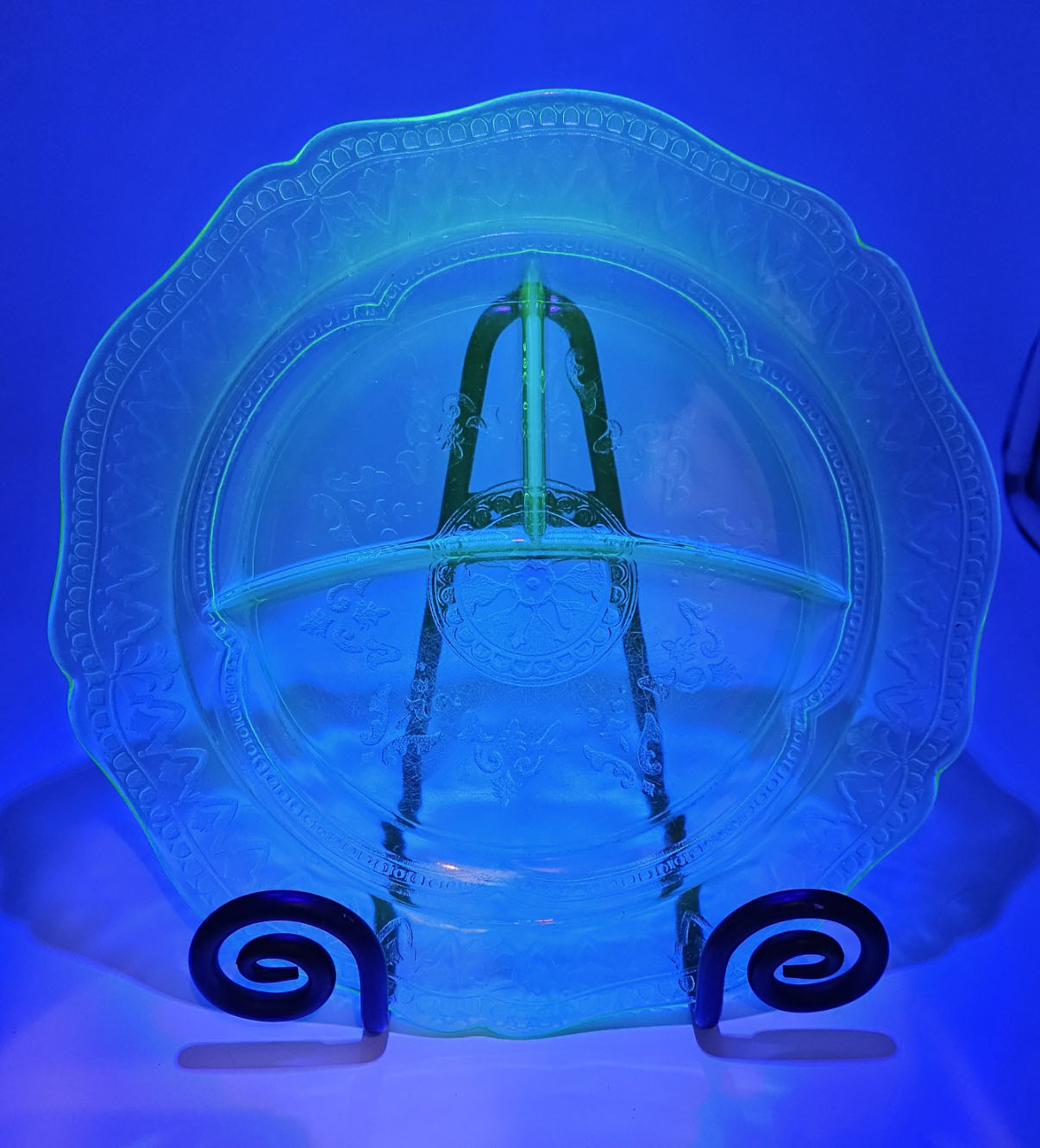 Uranium glass relish dish with decorative stand lit up by blacklight